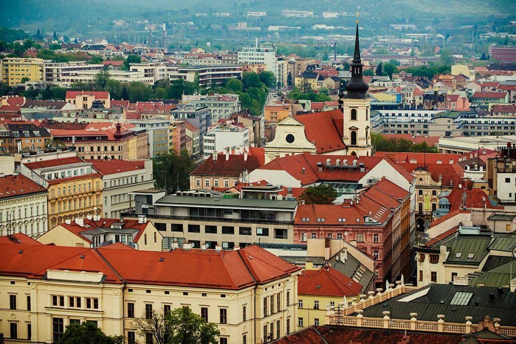 Vista aérea de una ciudad europea con edificios de tejados rojos, una iglesia con una alta aguja y una mezcla de arquitectura moderna e histórica.